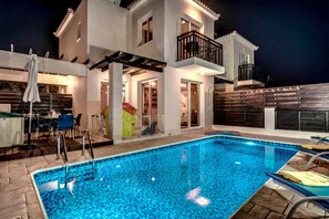 Una casa moderna de dos pisos con piscina, mobiliario de exterior y un balcón.