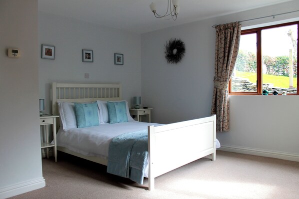 A bedroom with a white bed, bedside tables, a wall-mounted light fixture, and a window with curtains.