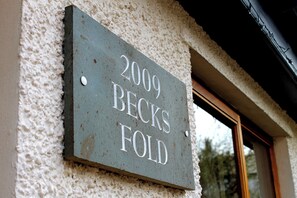 Et husnummer skilt med teksten '2009 BECKS FOLD' monteret på en væg med struktur.