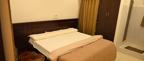 Una habitación de hotel con cama, una mesita, un armario y zona de ducha.