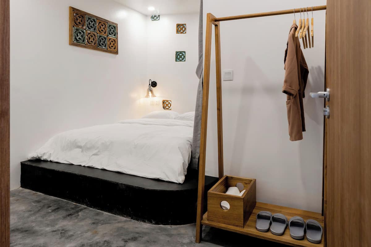 A bedroom with a bed, a wooden wardrobe, a nightstand, and a wall-mounted lamp.