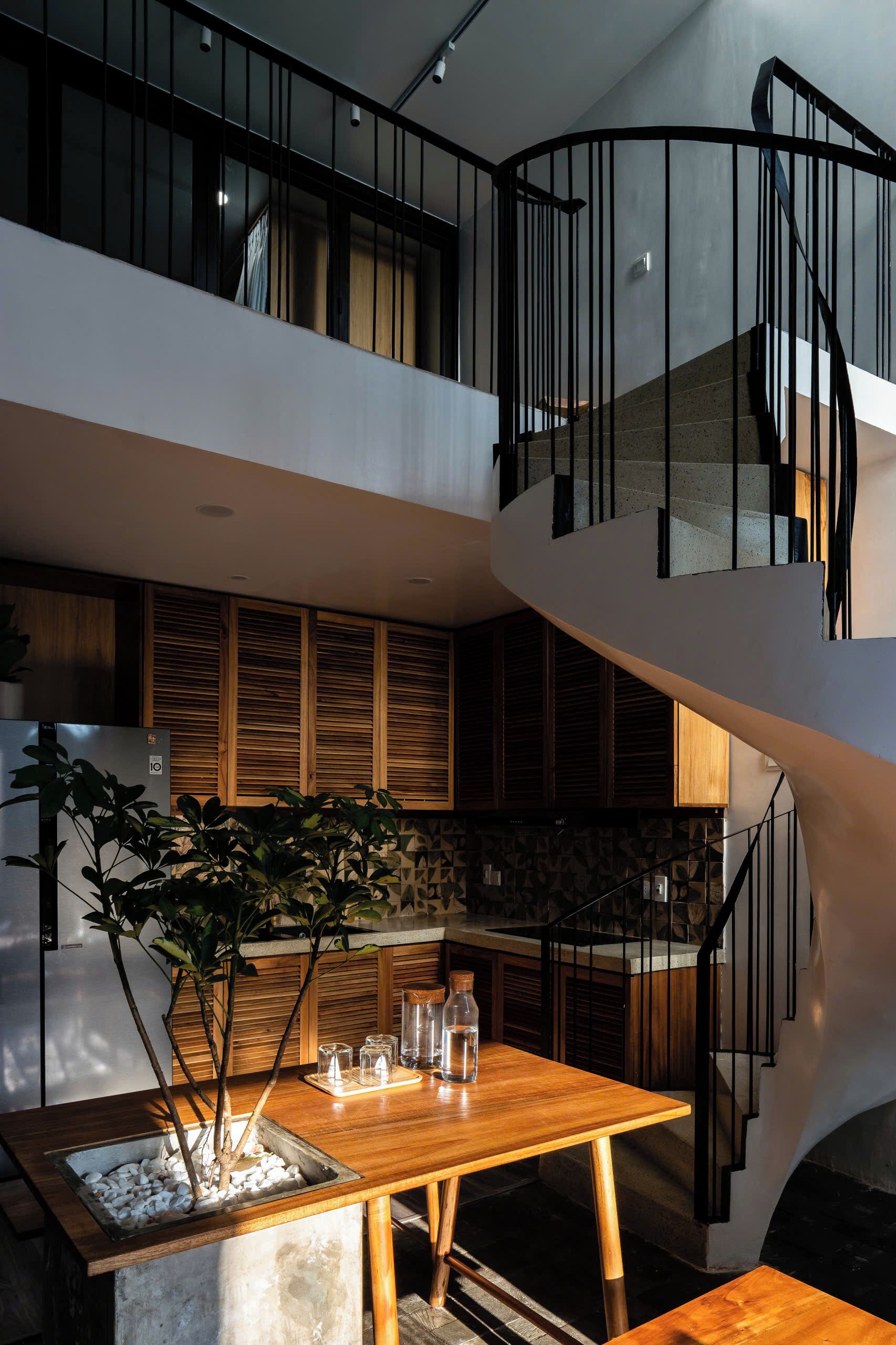 A modern kitchen with a wooden table and potted plants, a staircase with black railings, and a balcony with a view.