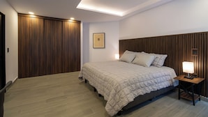 Een slaapkamer met een bed, houten paneelwanden, een nachtkastje met een lamp en een lijst met een afbeelding aan de muur.