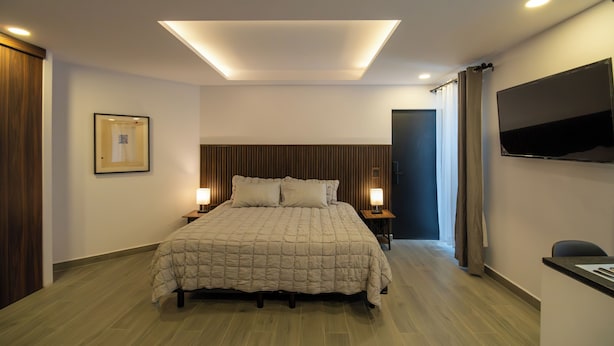 Een moderne hotelkamer met een groot bed, nachtlampjes, een flatscreen televisie en een houten hoofdbord.
