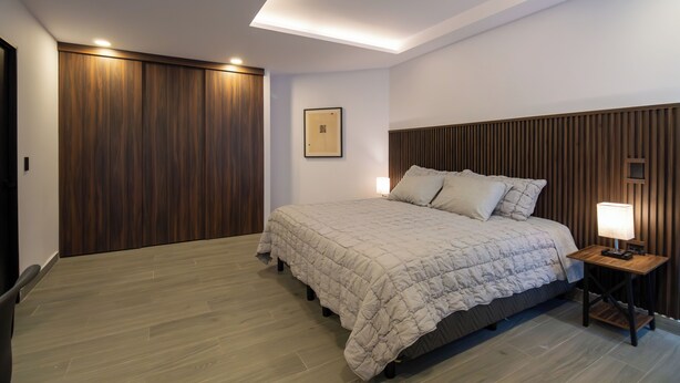 Een slaapkamer met een bed, houten paneelwanden, een nachtkastje met een lamp en een lijst met een afbeelding aan de muur.