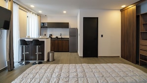 Habitació d'hotel moderna amb un llit gran, una cuina americana, una zona de bar i un armari.