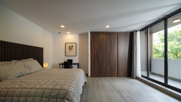 Une chambre moderne avec un grand lit, un bureau et une porte coulissante donnant sur un balcon.