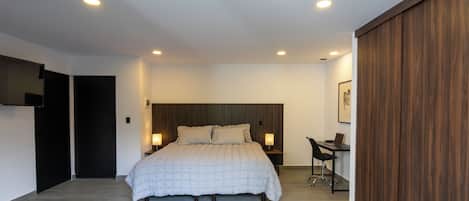 A modern bedroom with a large bed, bedside lamps, a desk, and a wardrobe.