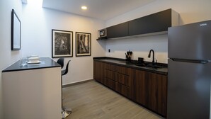 Une cuisine moderne équipée d’un four à micro-ondes encastré, d’un évier et d’un réfrigérateur. On y trouve des armoires en bois et un plan de travail noir. Deux tableaux encadrés sont accrochés au mur.