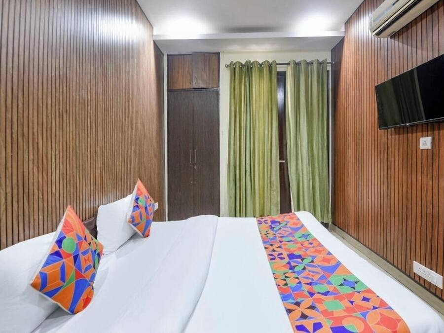 A hotel room with a bed, a TV mounted on the wall, and a wooden panel design.