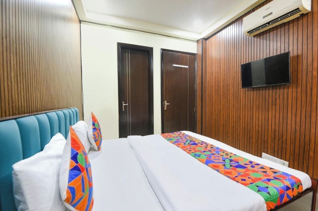A hotel room with a bed, two doors, a television mounted on the wall, and an air conditioning unit.