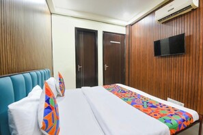A hotel room with a bed, two doors, a television mounted on the wall, and an air conditioning unit. - Hotel Red Leaf (Gurugram)