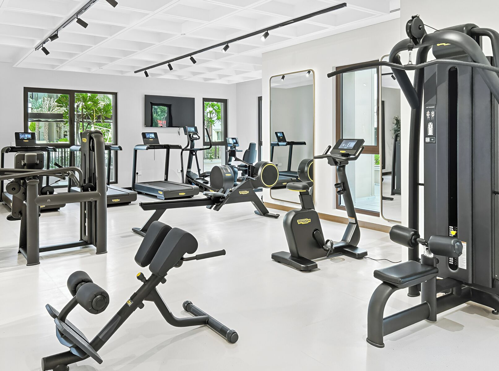 Un gimnasio moderno con diverso equipamiento de ejercicio, ventanas amplias y una distribución limpia y espaciosa.