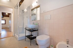 Een badkamer met douche, toilet, wastafel en spiegel.