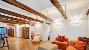 Un salon moderne avec des poutres apparentes, un canapé, un fauteuil, un téléviseur et un meuble orné de motifs.
