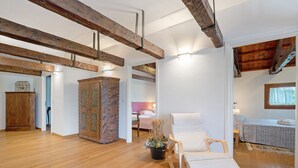 Une pi èce spacieuse avec des poutres apparentes, un plancher en bois, un fauteuil blanc, un lit recouvert d’une couvre-lit à motifs et une armoire.