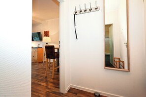A hallway with a wooden floor, a coat rack with hooks, a mirror, and a television mounted on the wall. - Vacation home Cumulus - Apartment 1 (Büsum)