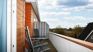 A balcony with a table and chairs, a white railing, and a view of the neighborhood. - Vacation home Cumulus - Apartment 4 (Büsum)