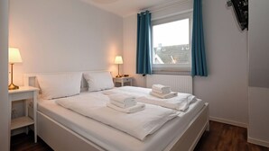 A clean, well-lit bedroom with a large bed, two bedside tables with lamps, a window with curtains, and a view of the outside. - Vacation home Cumulus - Apartment 4 (Büsum)