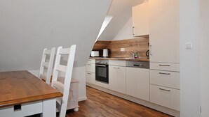 A modern kitchen with white cabinetry, a wooden dining table, and a built-in oven. - Vacation home Cumulus - Apartment 4 (Büsum)