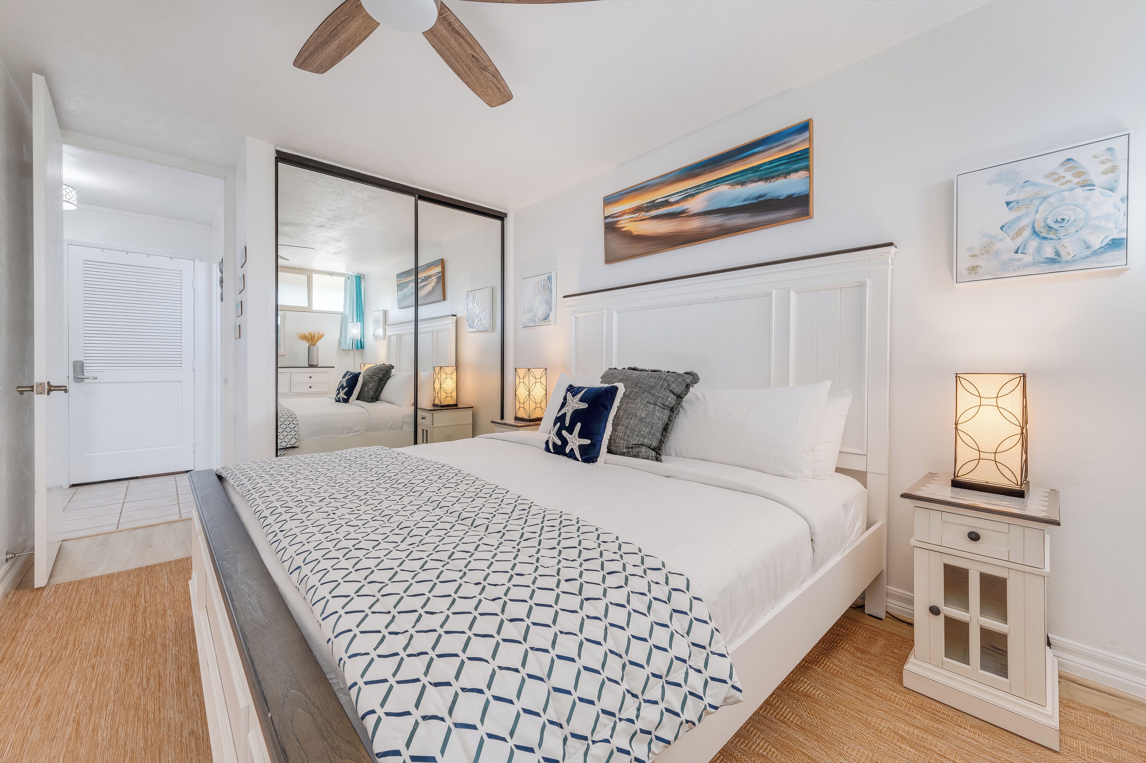 Bright bedroom featuring a king-size bed, coastal-inspired linens, and ceiling fan for a relaxing retreat.