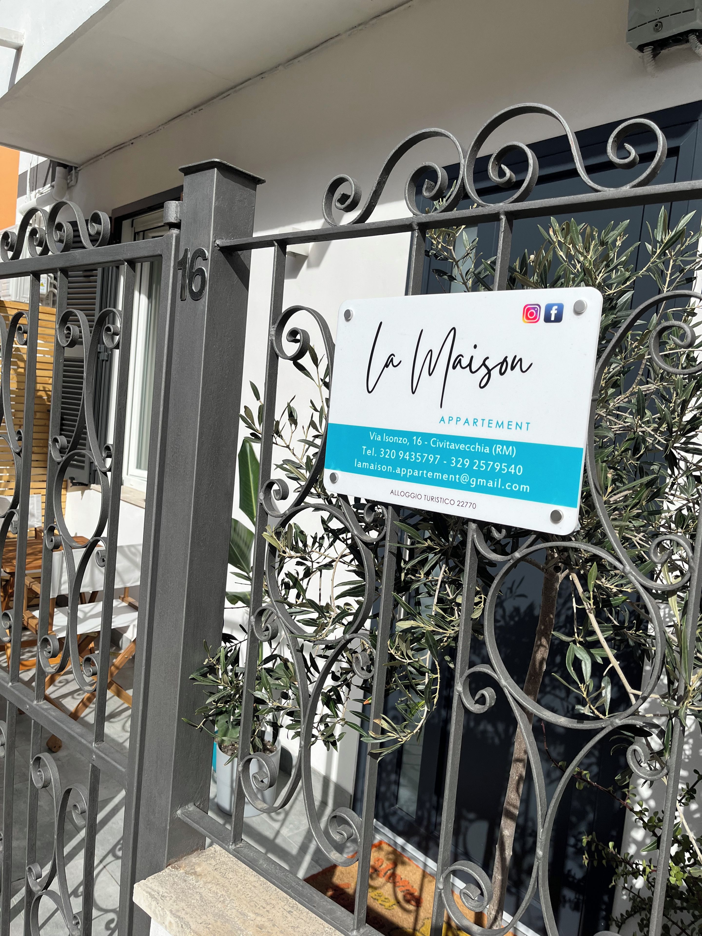 A gated entrance with a sign for 'La Maison Appartement' including contact information and a website.
