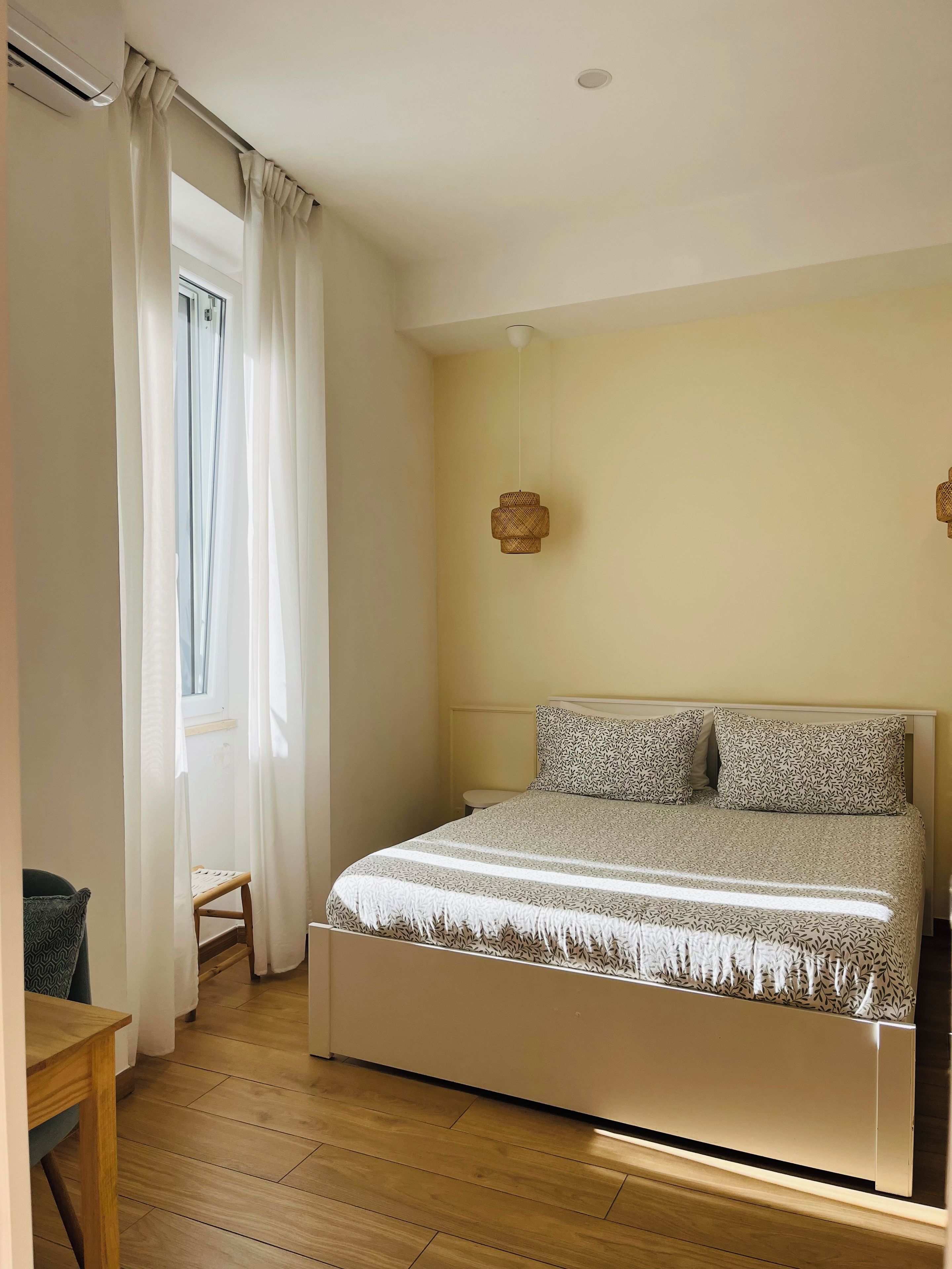 Una camera da letto con un letto, una finestra con tende, una lampada a sospensione e un termosifone.