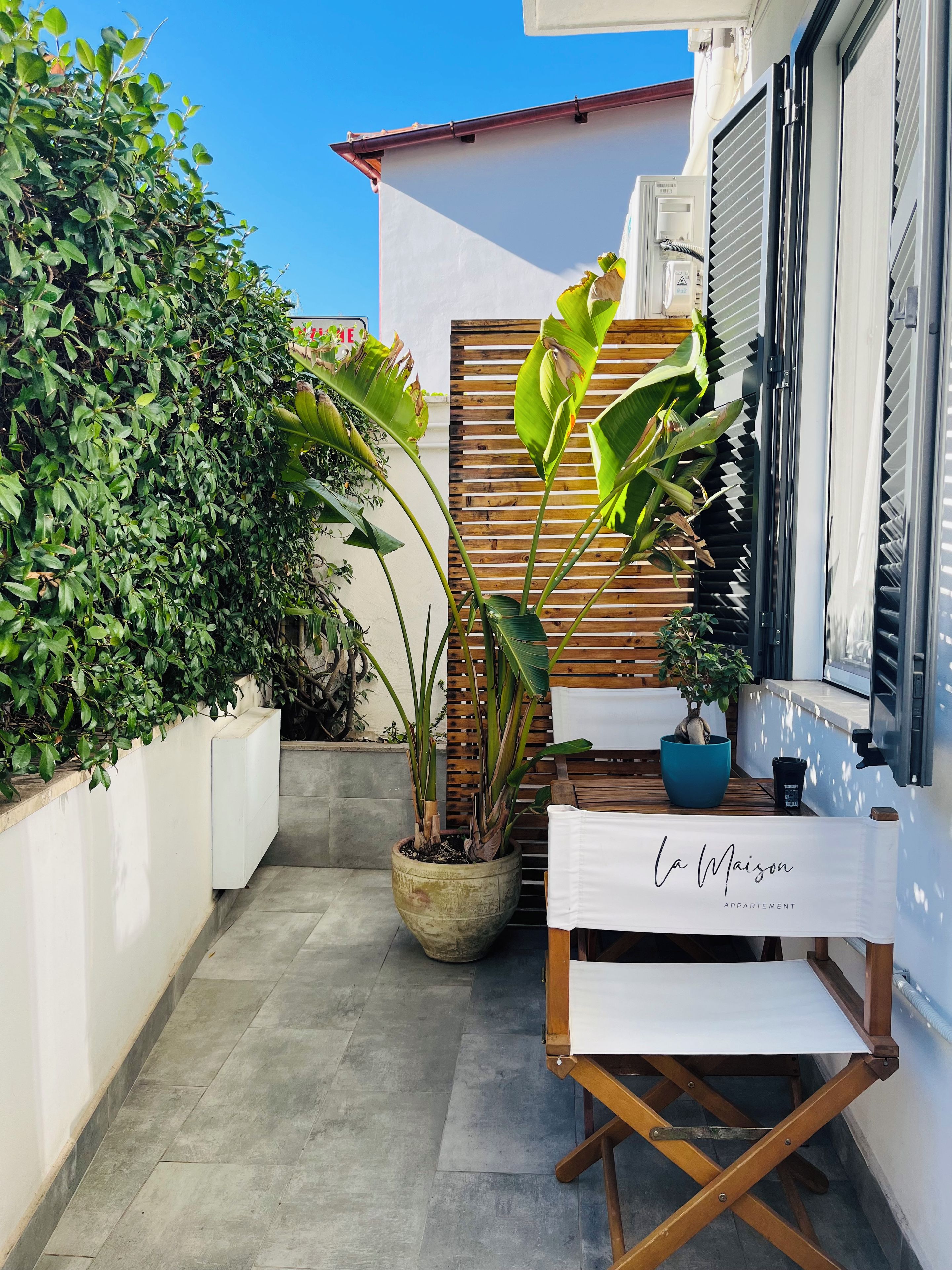 A courtyard with potted plants, a wooden bench, and a table with a sign.