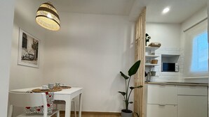A compact kitchen with white cabinetry, a dining table with chairs, a hanging light fixture, and a potted plant. - La Maison Appartement - 200m from the port (Civitavecchia)