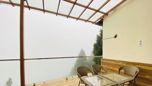 Un balcon agrémenté de meubles en osier et d’une table en verre, offrant une vue sur un paysage brumeux.