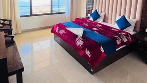 Une chambre spacieuse avec un grand lit, un ventilateur de plafond et une vue sur l’extérieur grâce à une grande fenêtre.