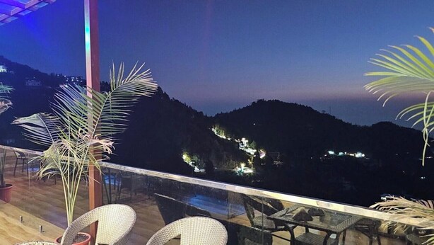 Un balcon agrémenté de plantes en pot, de meubles en osier et offrant une vue sur un paysage montagneux au crépuscule.