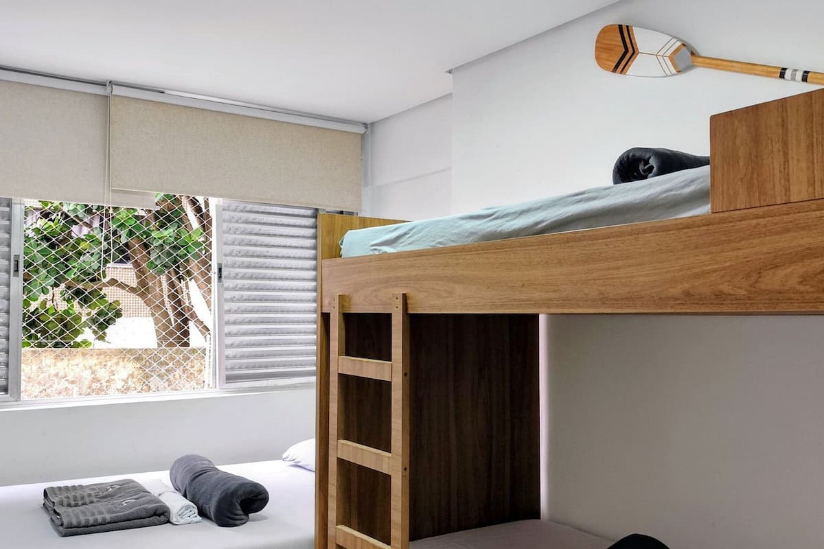 Ein Schlafraum mit Etagenbett, einer Leiter, einem Fenster und einer Deckenleuchte.