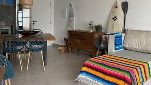 Ein Wohnzimmer mit Essbereich, einer Couch, einer bunten Decke, einem Surfbrett und einem Stand-Up-Paddle-Board.