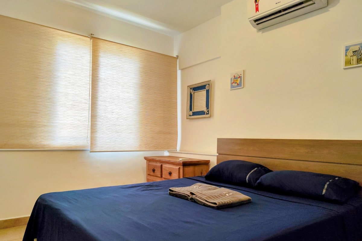 Ein Schlafzimmer mit einem Bett, einem Nachttisch aus Holz, einem kleinen Tisch und einer Wand-Klimaanlage.