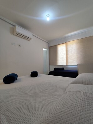 Camera d'albergo con due letti, una lampada a soffitto, condizionatore d'aria e finestra con persiane.
