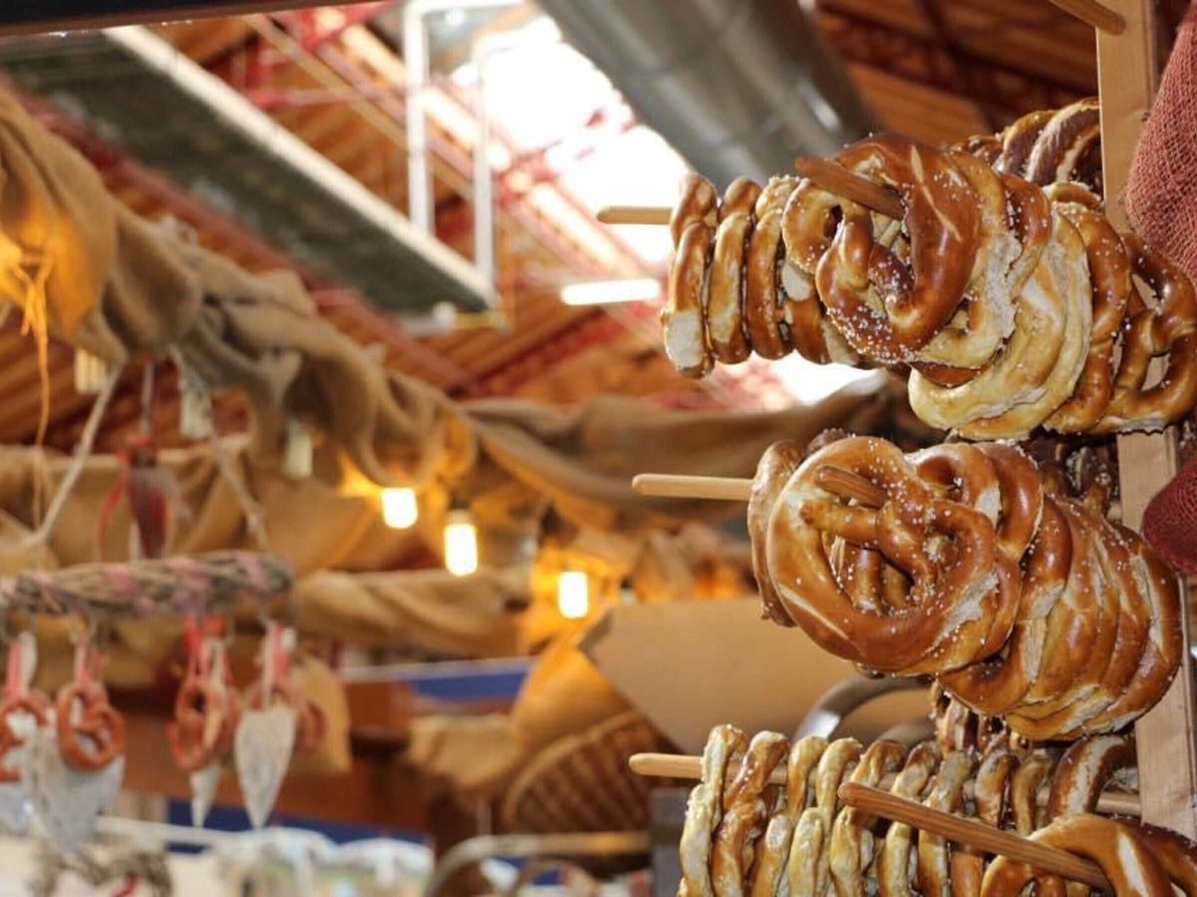A market stall with pretzels on skewers, surrounded by various food items and decorations.