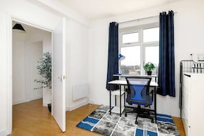 A room with a desk, chair, window, curtains, radiator, and a potted plant. - Charming 1-BR Apartment near Brick Lane Sleeps 3 (Greater London)