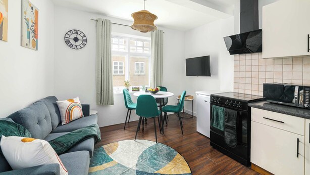 A compact living space with a sofa, dining table, chairs, a kitchen area with a stove and microwave, and a large window. - Charming 1-BR Apartment near Brick Lane Sleeps 3 (Greater London)