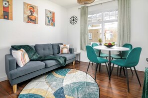 Un salon moderne avec un canapé gris, des fauteuils turquoise, une table ronde et un tapis à motifs.