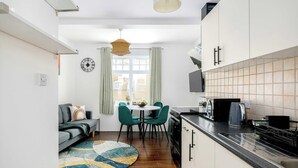 A compact kitchen with a dining area, a sofa, and a clock on the wall. - Charming 1-BR Apartment near Brick Lane Sleeps 3 (Greater London)