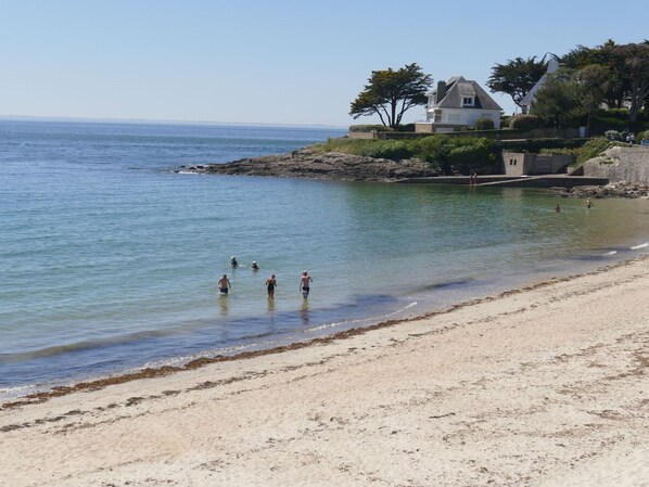 Una platja amb aigua cristal·lina, un tram de sorra i una casa amb jardí.