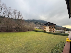 A multi-story building with balconies, a grassy lawn, and a mountainous backdrop. - Cozy apartment near slopes, balcony, parking (Bernex)