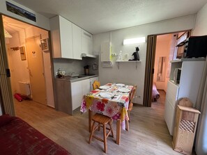 A compact kitchen with white cabinets, a dining table set with plates and a floral tablecloth, and a small refrigerator. - Cozy apartment near slopes, balcony, parking (Bernex)
