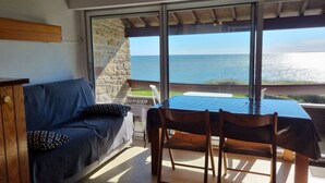 Una stanza con un divano, un tavolo, sedie, un muro in pietra e vista sul mare.