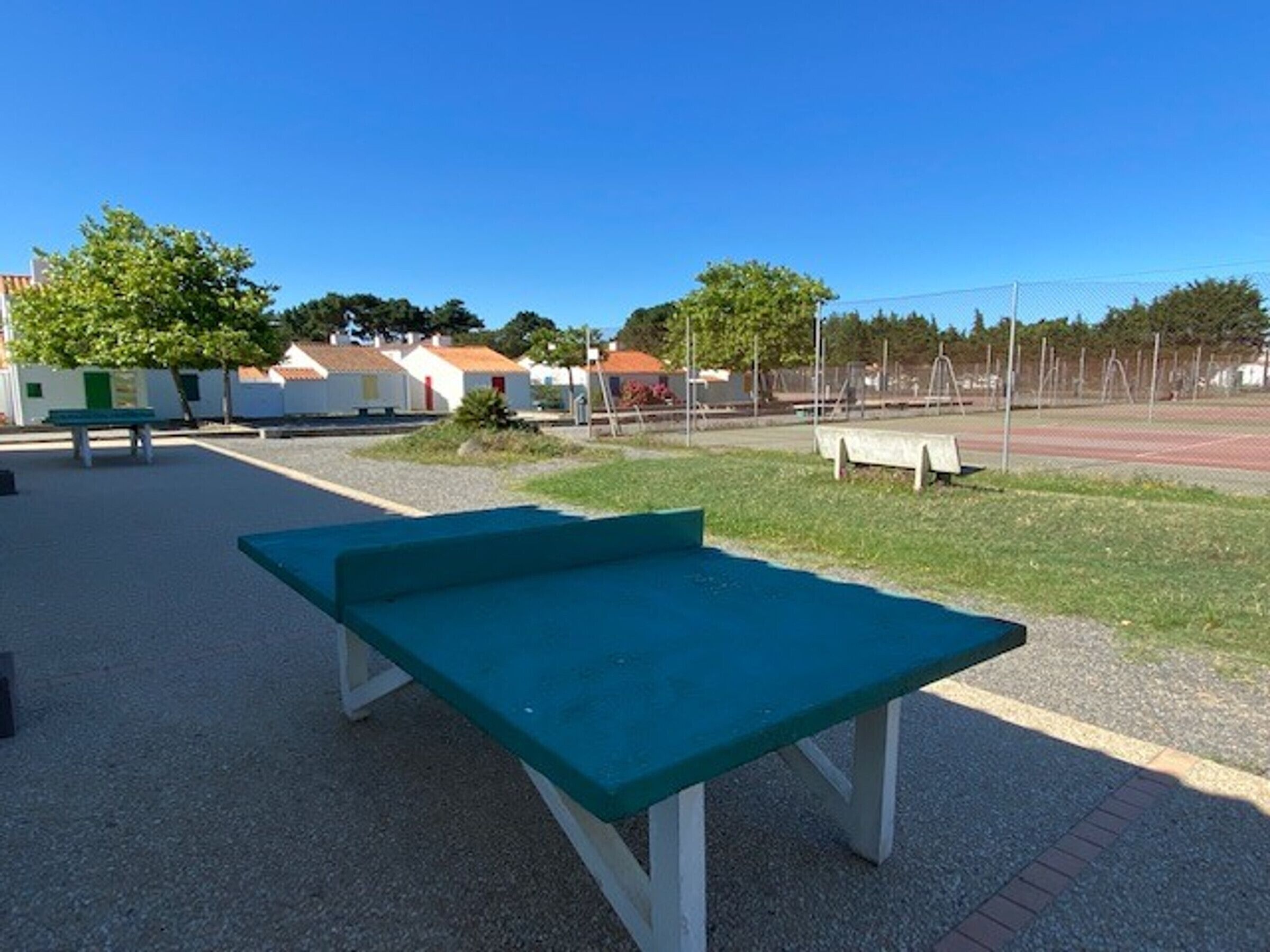 Een groene tafel in een park met een speeltuin en gebouwen op de achtergrond.