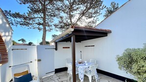 Eine Terrasse mit Steinboden, weißen Stühlen, einem Tisch und einer Pergola.