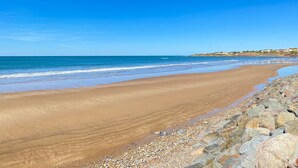 Ein weiter Sandstrand mit felsigem Ufer und blauem, wolkenlosem Himmel.