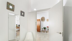 A hallway with a white chair, a door, and a mirror. - Quadruple Room (Arinaga)