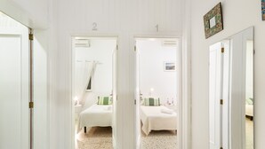 A hallway leading to two bedrooms, each with a bed, bedside table, and a mirror. - Quadruple Room (Arinaga)